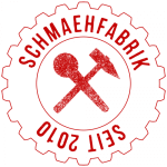Abb. Logo Schmähfabrik in From eines Zahnrades. In der Mitte Mirkofun und Hammer gekreuzt. Obere Beschriftung im Zahnrad: "Schmähfabrik", unter Beschriftung (auf dem Kopf stehend): "Seit 2010".